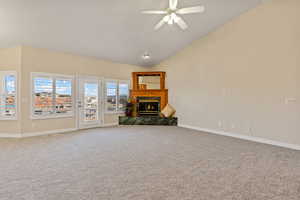 Unfurnished living room featuring a glass covered fireplace, carpet flooring, ceiling fan, and high vaulted ceiling