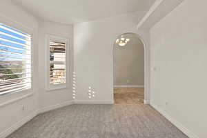 Spare room featuring arched walkways, light colored carpet, and a chandelier