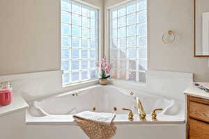 Full bath featuring vanity, a jetted tub, and a textured wall