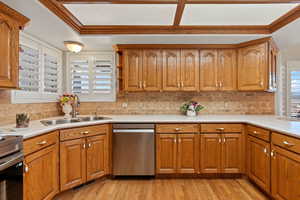 Kitchen with brown cabinets, appliances with stainless steel finishes, light countertops, light wood-type flooring, and backsplash