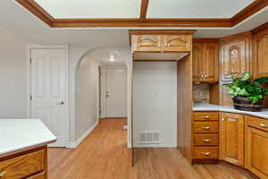 Kitchen with brown cabinets, crown molding, light countertops, a raised ceiling, and arched walkways