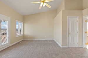Unfurnished bedroom with multiple windows, vaulted ceiling, light colored carpet, and a ceiling fan