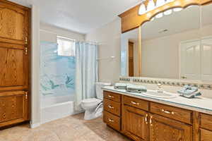 Full bath featuring shower / bath combination with curtain, a textured ceiling, vanity, light tile patterned floors, and decorative backsplash