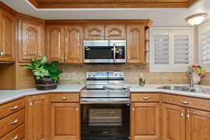 Kitchen with brown cabinetry, appliances with stainless steel finishes, light countertops, and crown molding