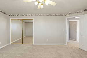 Unfurnished bedroom featuring light carpet, a closet, a textured ceiling, and a ceiling fan