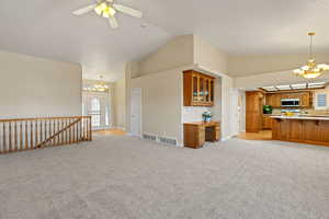 Unfurnished living room with a chandelier, light carpet, high vaulted ceiling, and ceiling fan