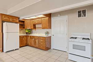 Kitchen with white appliances, light countertops, brown cabinetry, open shelves, and light tile patterned flooring