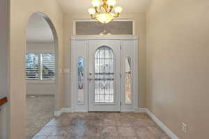 Tiled foyer with arched walkways, a chandelier, plenty of natural light, and carpet