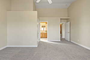 Unfurnished bedroom featuring light carpet, ensuite bath, high vaulted ceiling, and a ceiling fan