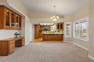 Kitchen with glass insert cabinets, a peninsula, brown cabinetry, hanging light fixtures, and light countertops