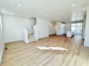 Unfurnished living room featuring stairs, a chandelier, light wood-type flooring, a textured ceiling, and recessed lighting