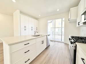 Kitchen featuring white cabinetry, appliances with stainless steel finishes, a center island with sink, light wood-style floors, and light stone countertops