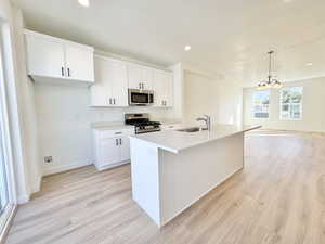 Kitchen featuring white cabinets, appliances with stainless steel finishes, a kitchen island with sink, hanging light fixtures, and light wood-style flooring