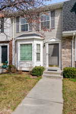 View of exterior entry featuring a shingled roof, a lawn, and brick siding