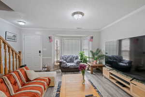 Living area with a textured ceiling, ornamental molding, stairs, and wood finished floors