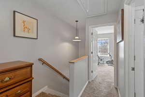 Hallway with light carpet, an upstairs landing, and attic access
