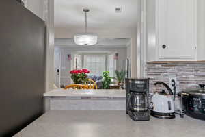 Kitchen view of light countertops, freestanding refrigerator, white cabinets, pendant lighting, and decorative backsplash