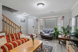 Living room featuring stairway, ornamental molding, a textured ceiling, and wood finished floors