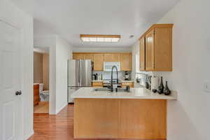 Kitchen featuring light countertops, freestanding refrigerator, a peninsula, light wood finished floors, and white microwave