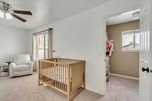 Bedroom featuring light carpet, a nursery area, and ceiling fan