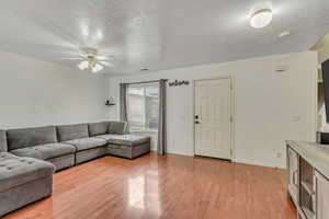 Living area with a textured ceiling, ceiling fan, and light wood-style flooring