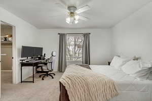 Bedroom with an office area, light carpet, and a ceiling fan