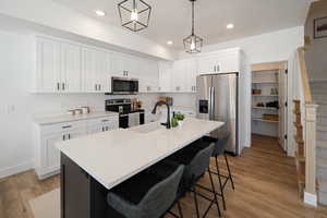 Kitchen with white cabinets, appliances with stainless steel finishes, light wood-style flooring, a breakfast bar, and decorative light fixtures