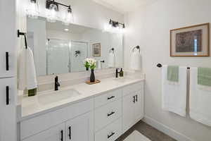 Full bath with a stall shower, double vanity, and dark tile patterned flooring