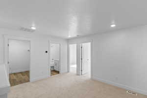 Unfurnished bedroom with a walk in closet, light colored carpet, recessed lighting, and connected bathroom