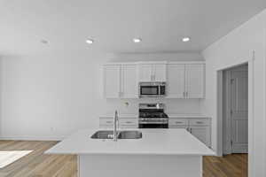 Kitchen featuring white cabinets, appliances with stainless steel finishes, a center island with sink, recessed lighting, and light wood finished floors