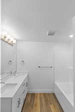 Bathroom with double vanity, light wood-style floors, tub / shower combination, and a textured ceiling