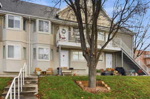 View of front of house featuring a balcony, stucco siding, stairway, and a front yard