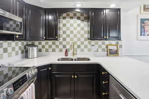 Kitchen featuring appliances with stainless steel finishes, tasteful backsplash, light stone counters, and dark cabinetry
