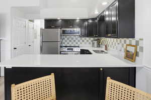 Kitchen with dark cabinets, stainless steel appliances, light stone countertops, tasteful backsplash, and a peninsula