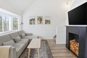 Living room with light wood finished floors, stairs, high vaulted ceiling, and a fireplace