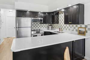 Kitchen featuring dark cabinetry, stainless steel appliances, light stone counters, backsplash, and recessed lighting