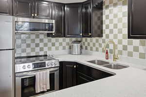 Kitchen with appliances with stainless steel finishes, light stone countertops, backsplash, and dark cabinets
