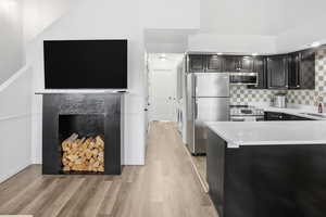 Kitchen featuring stainless steel appliances, light stone counters, dark cabinets, light wood-style flooring, and tasteful backsplash