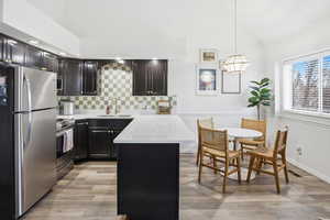 Kitchen with appliances with stainless steel finishes, a peninsula, decorative backsplash, dark cabinets, and pendant lighting