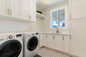 Laundry room with cabinet space, light floors, washer and clothes dryer, and a chandelier