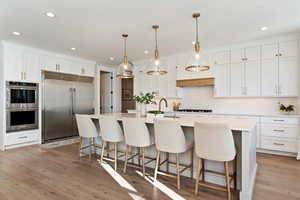 Kitchen with stainless steel appliances, white cabinets, a breakfast bar, a kitchen island with sink, and recessed lighting
