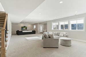 Living room with stairs, light colored carpet, and recessed lighting