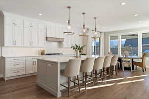 Kitchen with a breakfast bar area, white cabinetry, decorative light fixtures, a large island with sink, and dark wood-style flooring