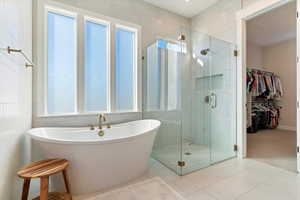 Bathroom with a freestanding tub, a stall shower, a walk in closet, carpet flooring, and tile walls