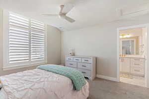 Bedroom with light colored carpet, ceiling fan, and connected bathroom