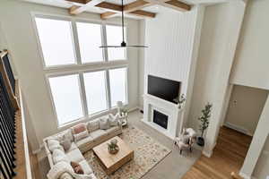 Living room with a fireplace with flush hearth, healthy amount of natural light, beam ceiling, ceiling fan, and coffered ceiling