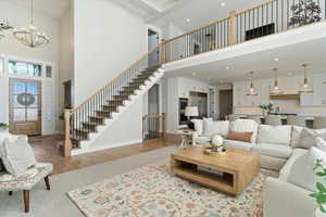 Living room featuring a towering ceiling, a chandelier, stairway, wood finished floors, and recessed lighting