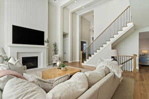 Living room with a high ceiling, a chandelier, a fireplace with flush hearth, wood finished floors, and stairs