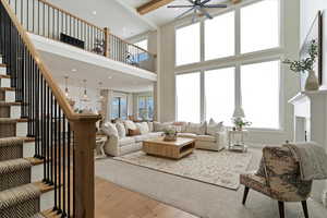 Living room featuring stairway, a towering ceiling, light wood-style floors, ceiling fan, and beam ceiling