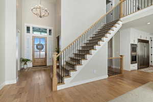 Foyer featuring a towering ceiling, light wood-type flooring, a chandelier, and stairway